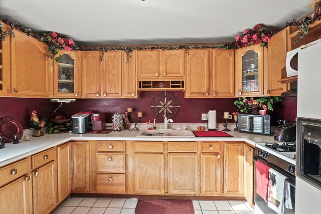 kitchen with glass insert cabinets, light countertops, gas range oven, light tile patterned floors, and a sink