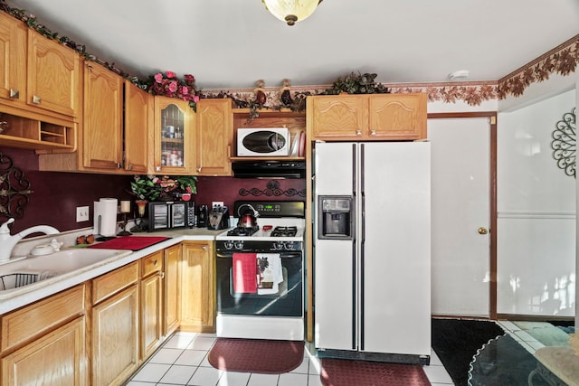 kitchen with a sink, white appliances, light tile patterned flooring, light countertops, and glass insert cabinets