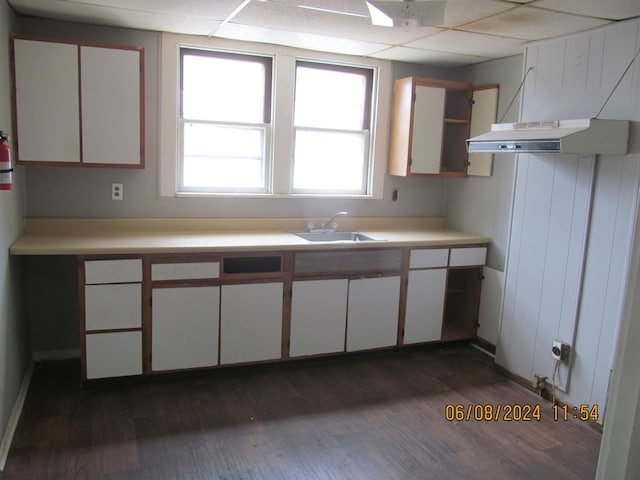 kitchen with a drop ceiling, under cabinet range hood, white cabinetry, light countertops, and dark wood finished floors