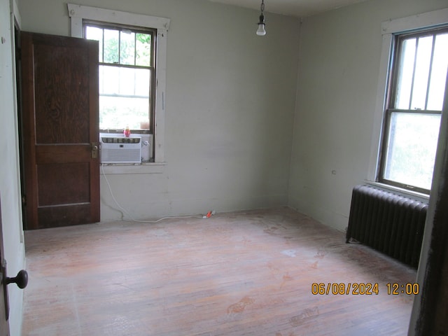 unfurnished room featuring light wood-type flooring, radiator heating unit, and a healthy amount of sunlight