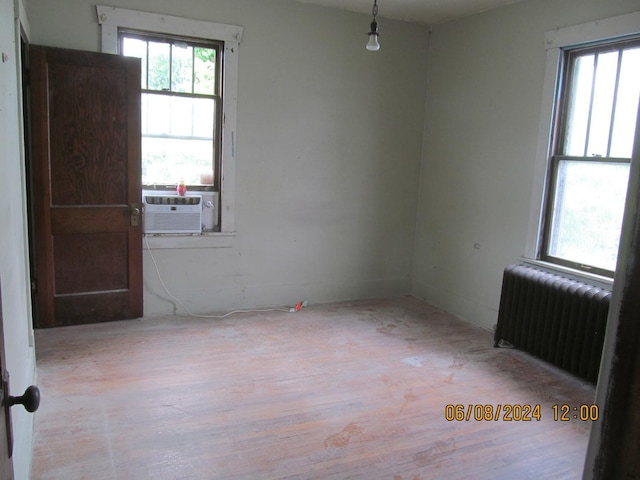 empty room featuring radiator heating unit, plenty of natural light, cooling unit, and light wood-style flooring