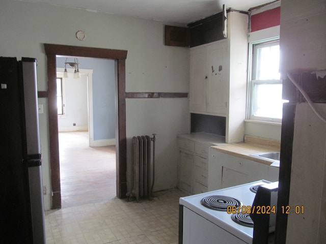 kitchen with light tile patterned floors, stainless steel refrigerator, radiator, white cabinetry, and stove