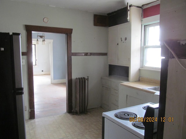 kitchen with light countertops, electric range, radiator heating unit, freestanding refrigerator, and white cabinets