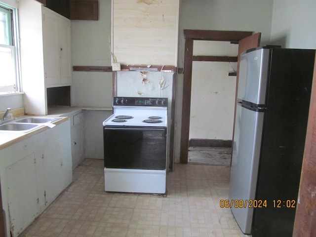 kitchen with electric range, a sink, white cabinetry, light countertops, and freestanding refrigerator