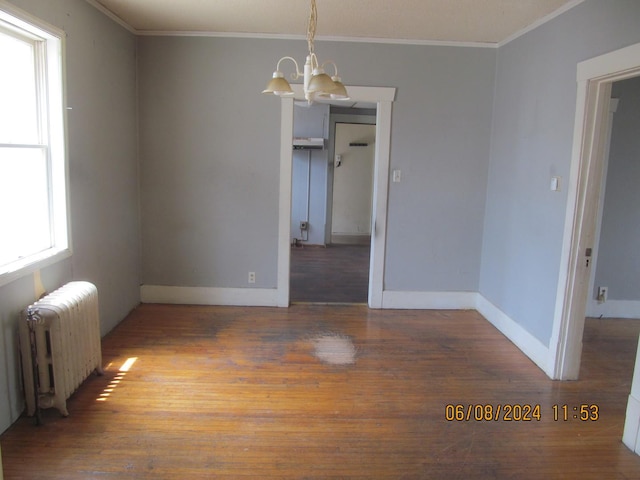 empty room featuring crown molding, an inviting chandelier, wood finished floors, and radiator