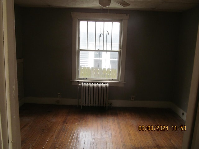 spare room with radiator, ceiling fan, baseboards, and dark wood-type flooring