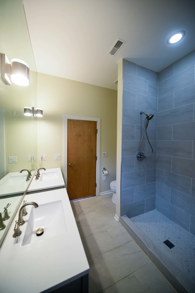 bathroom with toilet, a tile shower, tile patterned flooring, and vanity