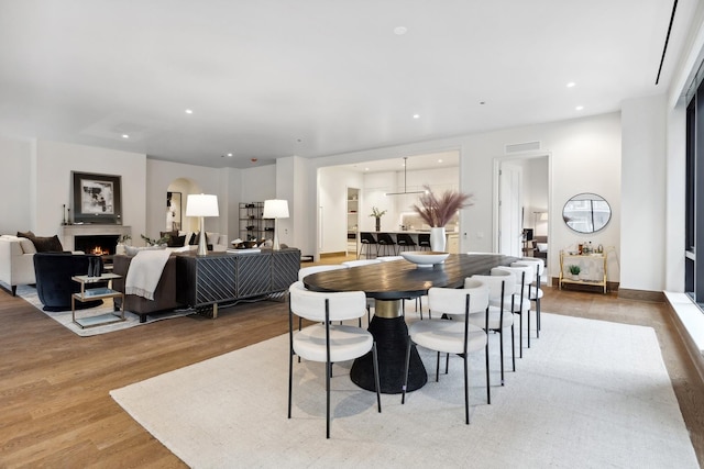 dining area featuring arched walkways, recessed lighting, visible vents, wood finished floors, and a lit fireplace