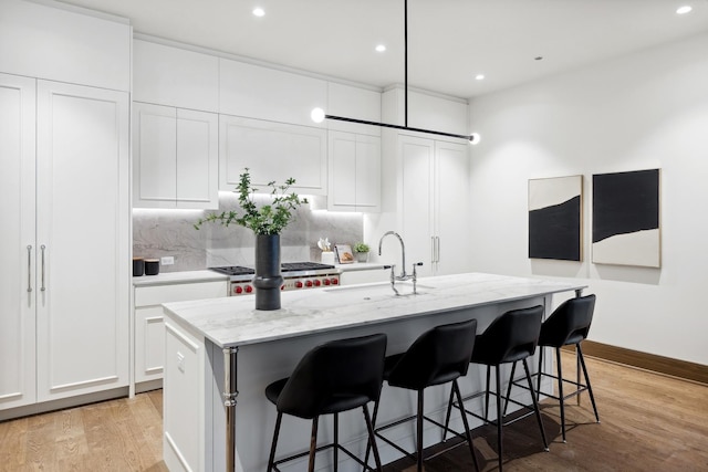 kitchen featuring light stone counters, light wood-type flooring, a center island with sink, and decorative backsplash