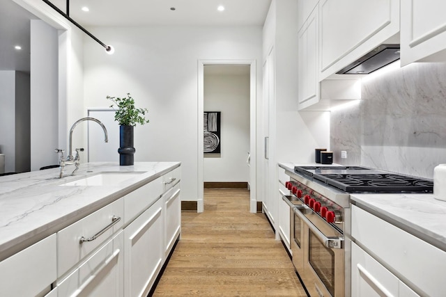 kitchen with range with two ovens, backsplash, light wood-style flooring, white cabinetry, and a sink