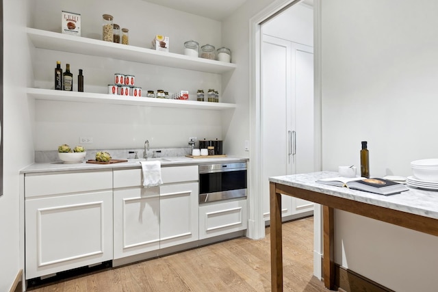 bar with light wood-style flooring, a sink, and stainless steel oven