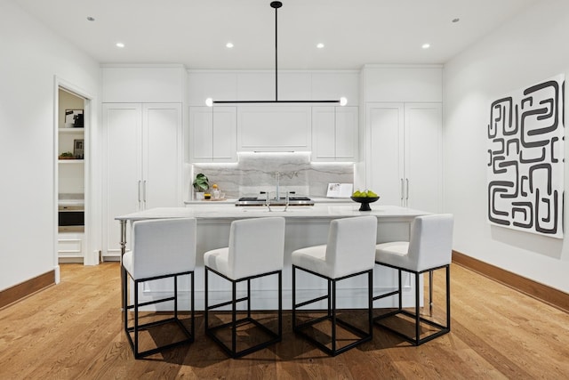 21 N May St Unit 402, Chicago, IL 60607 - kitchen featuring light wood-type flooring, white cabinets, an island with sink, backsplash, and light countertops