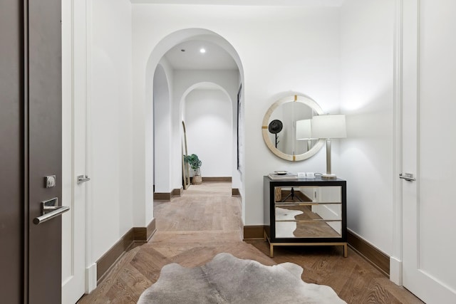 corridor with arched walkways, wood finished floors, and baseboards