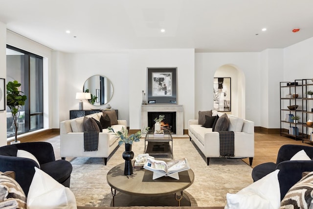 living room with a warm lit fireplace, baseboards, arched walkways, and recessed lighting