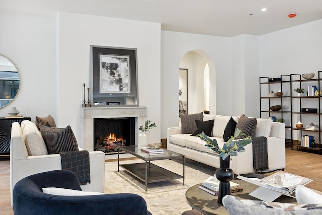 living area with a warm lit fireplace, arched walkways, wood finished floors, and recessed lighting