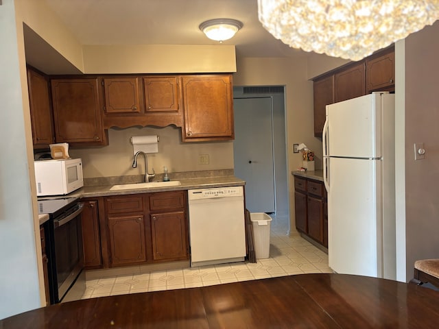 kitchen with sink, an inviting chandelier, light hardwood / wood-style flooring, and white appliances