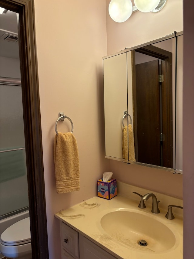 bathroom with toilet, vanity, and a shower with shower door