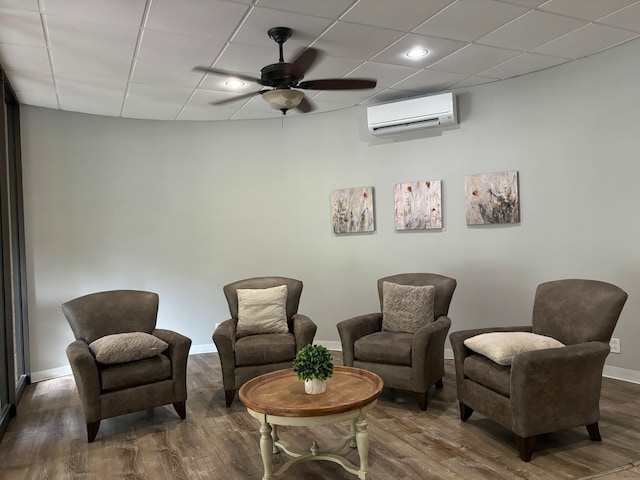 sitting room with dark hardwood / wood-style flooring, a wall mounted AC, a paneled ceiling, and ceiling fan