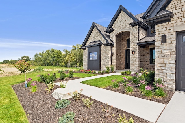 view of front of property featuring a front yard, stone siding, brick siding, and roof with shingles