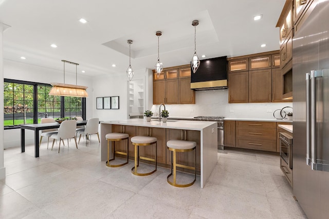 kitchen with pendant lighting, a center island with sink, wall chimney range hood, and high end appliances