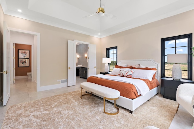 bedroom with light tile patterned floors, baseboards, a raised ceiling, and connected bathroom