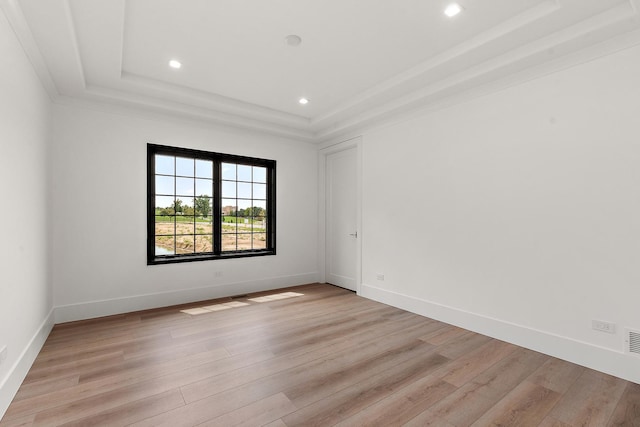 spare room featuring recessed lighting, a raised ceiling, light wood-style flooring, and baseboards