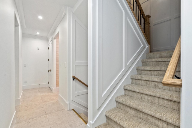 staircase featuring baseboards, a decorative wall, crown molding, and recessed lighting