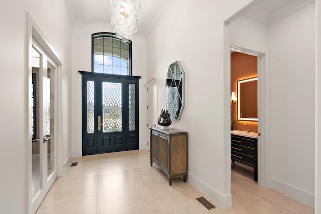 entrance foyer featuring crown molding, a chandelier, visible vents, and baseboards