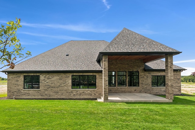 back of property featuring a yard, roof with shingles, a patio, and brick siding