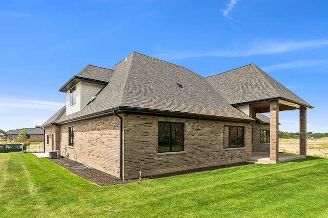 rear view of house with roof with shingles, a lawn, cooling unit, and brick siding