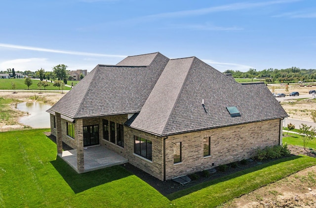 back of property featuring a yard, roof with shingles, a patio, and brick siding