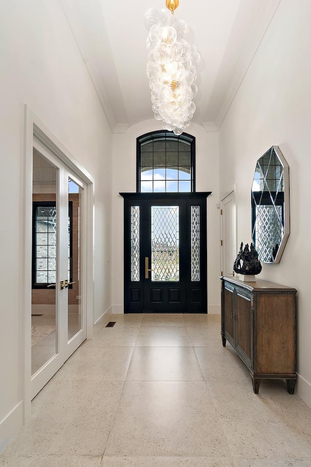 foyer entrance featuring baseboards, crown molding, french doors, light speckled floor, and a notable chandelier