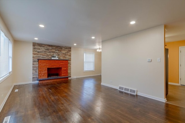 unfurnished living room featuring a stone fireplace, plenty of natural light, and dark hardwood / wood-style flooring