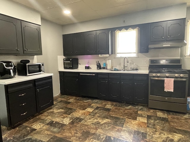 kitchen featuring tasteful backsplash, light countertops, appliances with stainless steel finishes, a sink, and under cabinet range hood