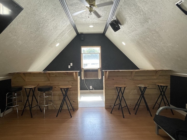 additional living space with a textured ceiling, wooden walls, wood finished floors, vaulted ceiling, and a bar