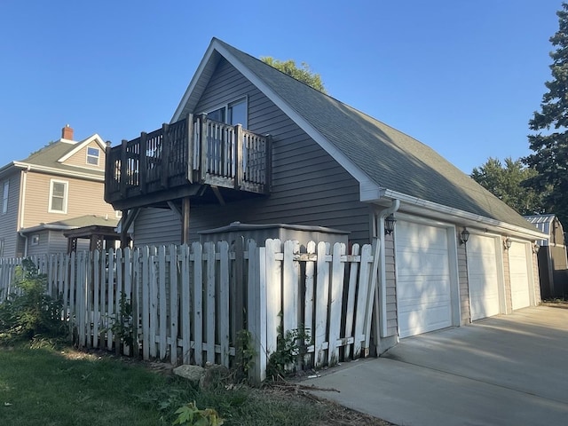 view of side of home featuring a balcony, a detached garage, fence, and roof with shingles