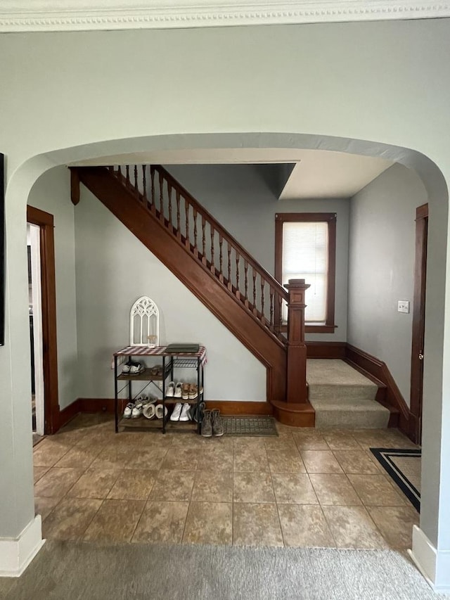 staircase with arched walkways, baseboards, and tile patterned floors