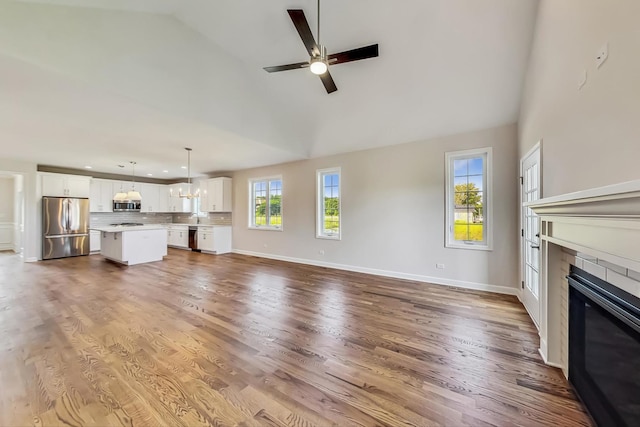 unfurnished living room with hardwood / wood-style floors, high vaulted ceiling, sink, a fireplace, and ceiling fan