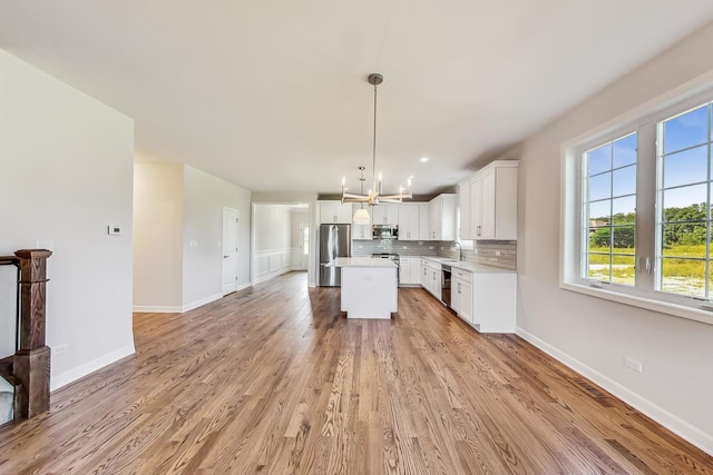 kitchen featuring appliances with stainless steel finishes, light hardwood / wood-style floors, a kitchen island, and tasteful backsplash