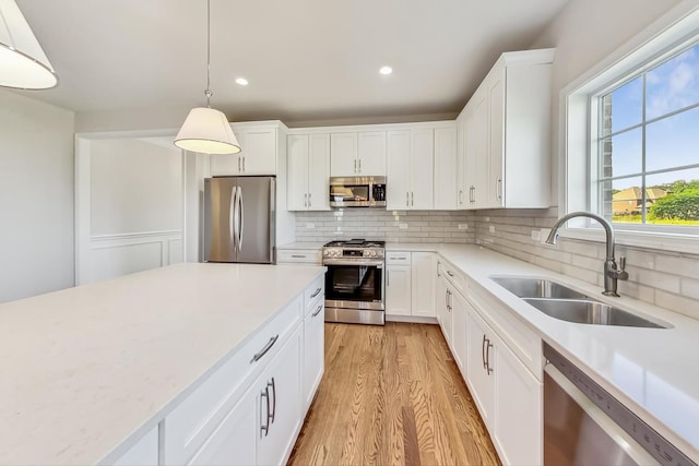 kitchen featuring appliances with stainless steel finishes, light hardwood / wood-style flooring, backsplash, white cabinetry, and sink