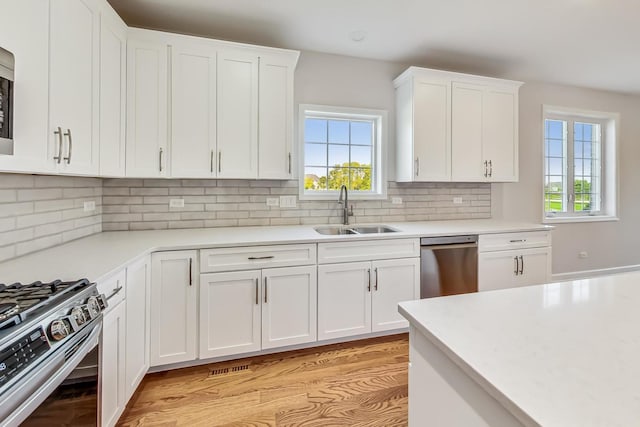 kitchen with light hardwood / wood-style flooring, tasteful backsplash, white cabinets, dishwasher, and sink