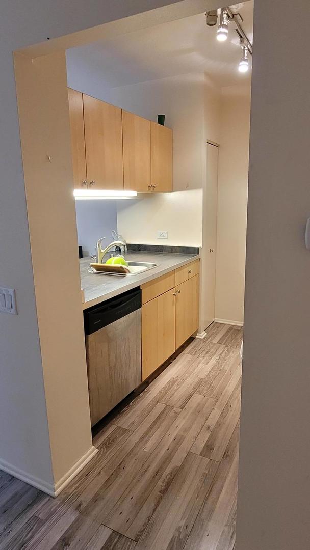 kitchen with sink, stainless steel dishwasher, light brown cabinets, and light wood-type flooring