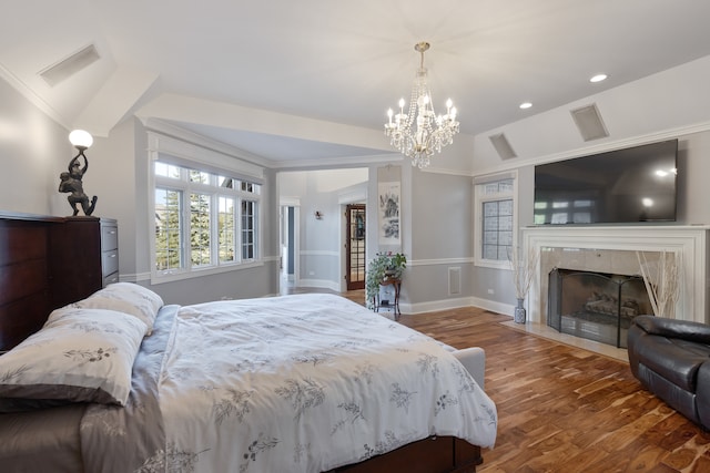 bedroom featuring wood-type flooring, a tile fireplace, a chandelier, and ornamental molding