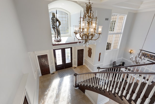 foyer entrance with ornamental molding, a high ceiling, and a notable chandelier