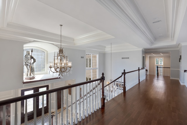 corridor with ornamental molding, a raised ceiling, a notable chandelier, and dark hardwood / wood-style flooring