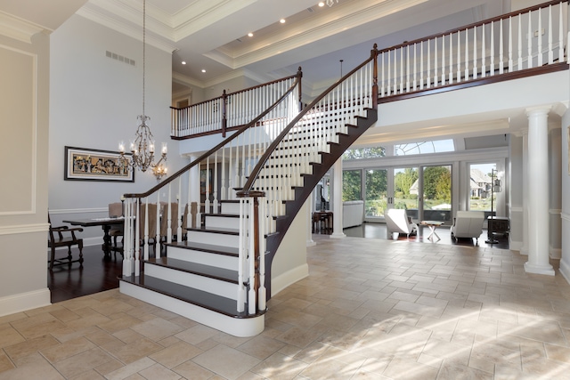 staircase with ornate columns, crown molding, a notable chandelier, and a towering ceiling