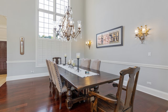 dining space with dark wood-type flooring, a notable chandelier, and a towering ceiling