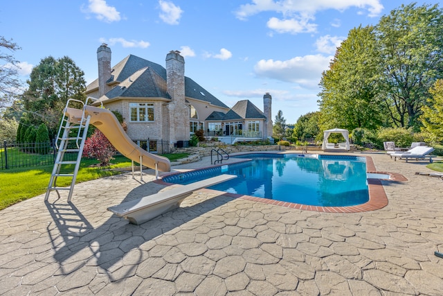 view of pool with a water slide, a diving board, and a patio