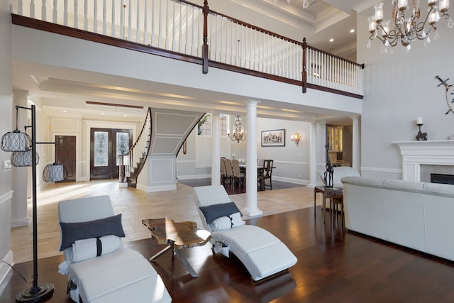 living room with decorative columns, hardwood / wood-style flooring, a notable chandelier, and a towering ceiling