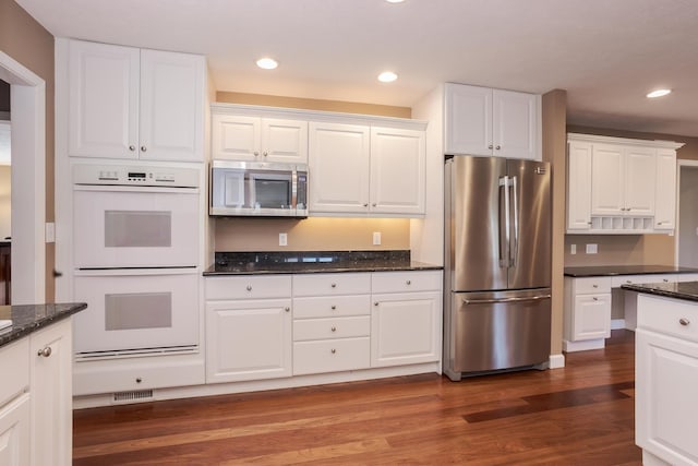 kitchen with white cabinets, appliances with stainless steel finishes, dark wood-type flooring, and dark stone countertops